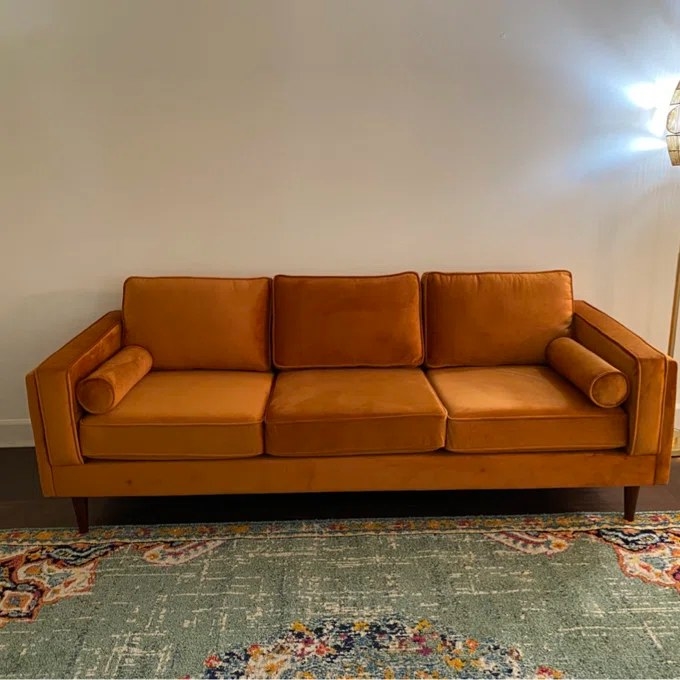 An orange velvet sofa with three cushions and two matching round pillows in a living room