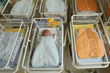 A 4-day-old newborn baby lies in a baby bed in the maternity ward of a hospital.