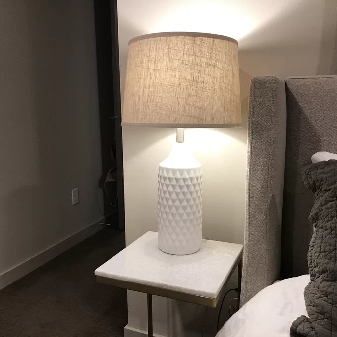 The lamp with a textured base and burlap shade on a bedside table