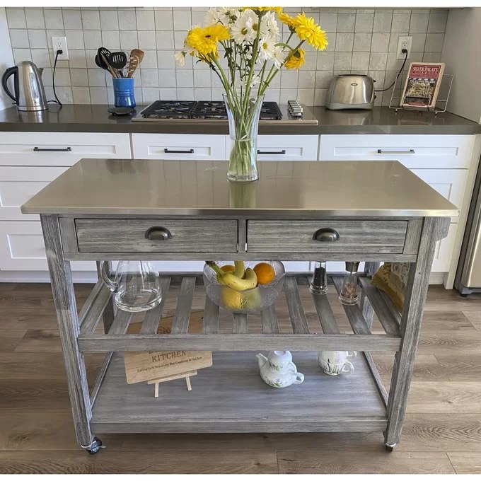 a reviewer photo of the kitchen island with flowers in a vase, fruit bowl, and teapot set underneath