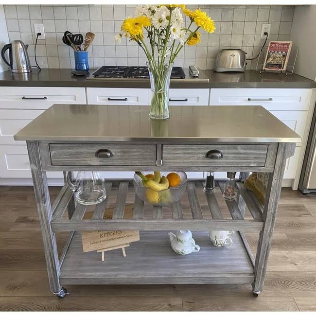 A reviewer photo of the kitchen island with flowers in a vase on top, fruit bowl on the first shelf, and teapot set on the second shelf