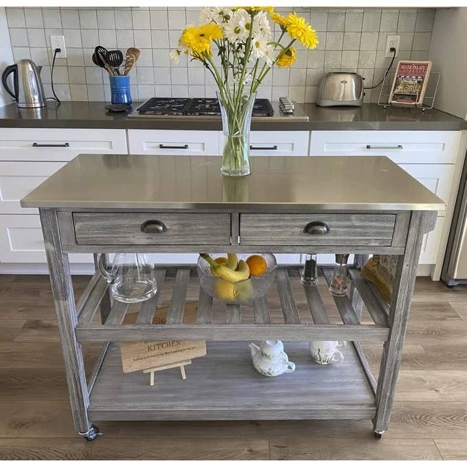 The cart on wheels with a stainless steel top, two drawers, and two open shelves