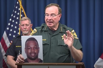 A sheriff is shown holding up a photo of an arrested individual