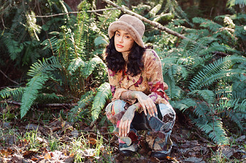 Kehlani crouching in a wooded area.