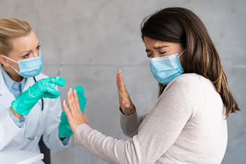A woman refusing to get vaccinated by a doctor holding a needle.