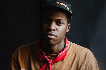 Canadian R&B star Daniel Caesar posing in cap and red bandana
