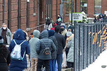 People wearing face masks line up to enter a COVID-19 assessment center in Toronto