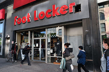 People wearing protective masks walk past a Foot Locker store