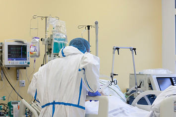 COVID-19 nurse talking to a patient, all-over protective clothing in intensive care unit