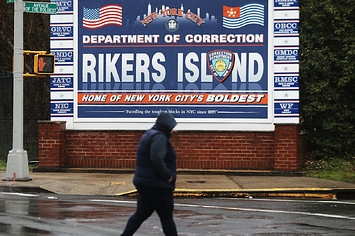 A woman walks by a sign at the entrance to Rikers Island.