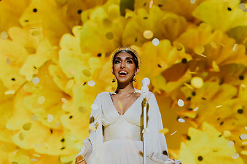 Rupi Kaur standing in front of a yellow flower