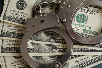 In this photo illustrations handcuffs and hundred us dollar banknotes seen displayed.