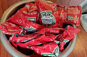 Close-up of container of Heinz brand ketchup packets in restaurant setting.