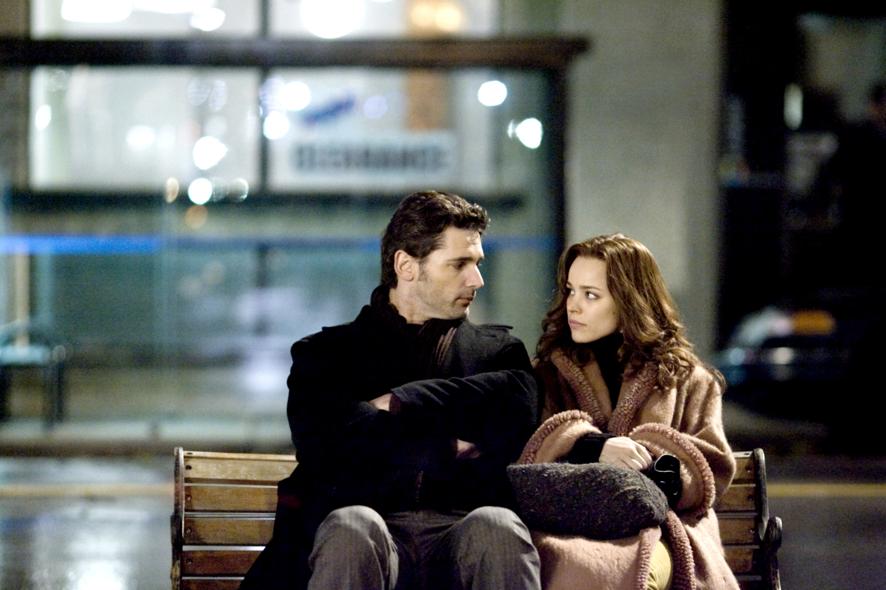 a man and a woman sit on a park bench and look at each other
