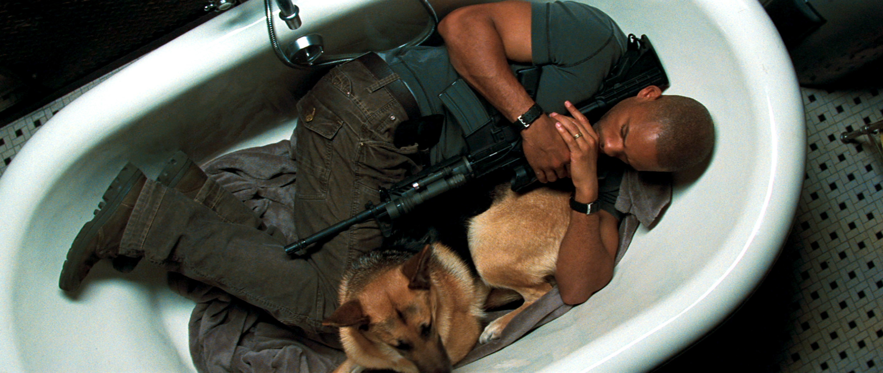 a man holding a gun and lying in an empty bathtub with a dog