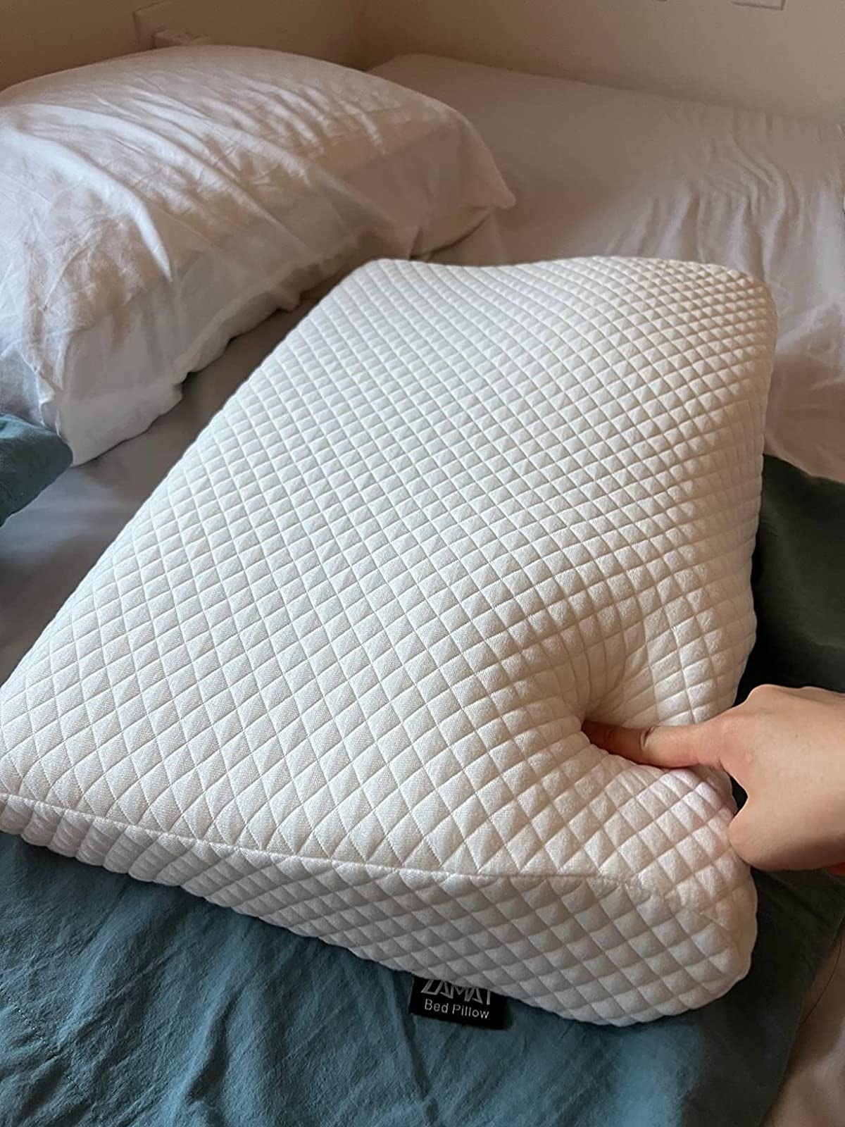 reviewer presses down finger into white cushy memory foam pillow on bed