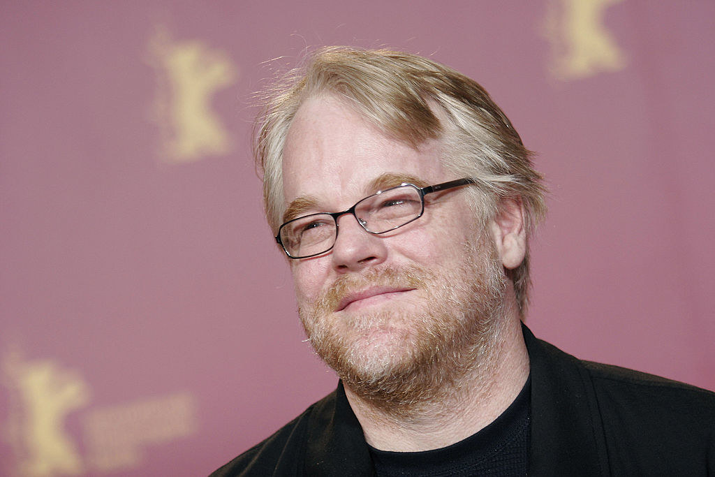 Philip Seymour Hoffman on a red carpet wearing glasses looking up smiling