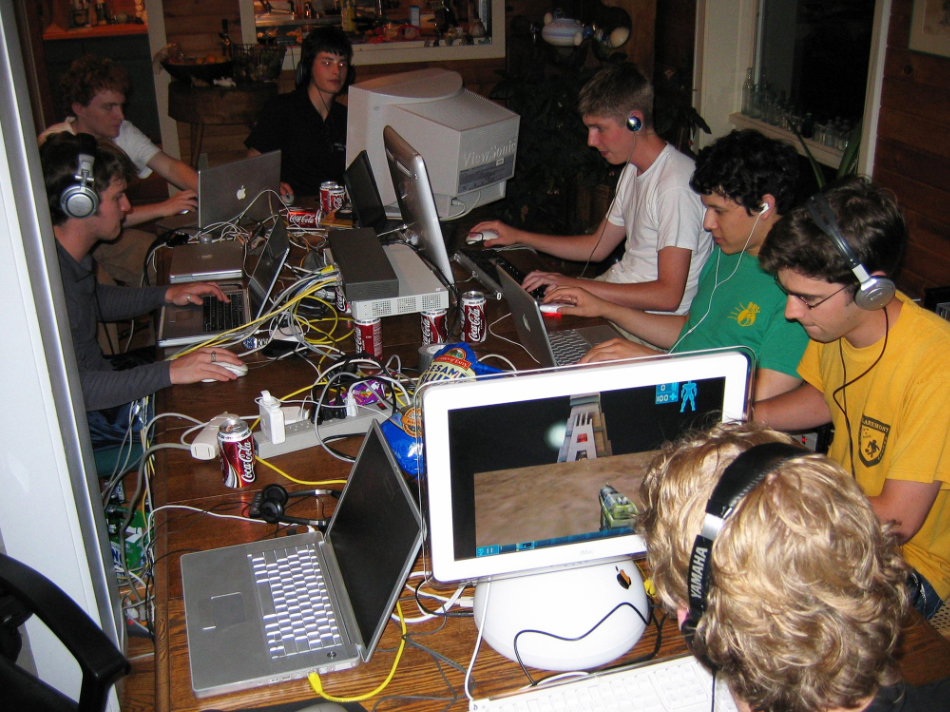 a bunch of fellas wearing headphones in front of desktop computers at one table