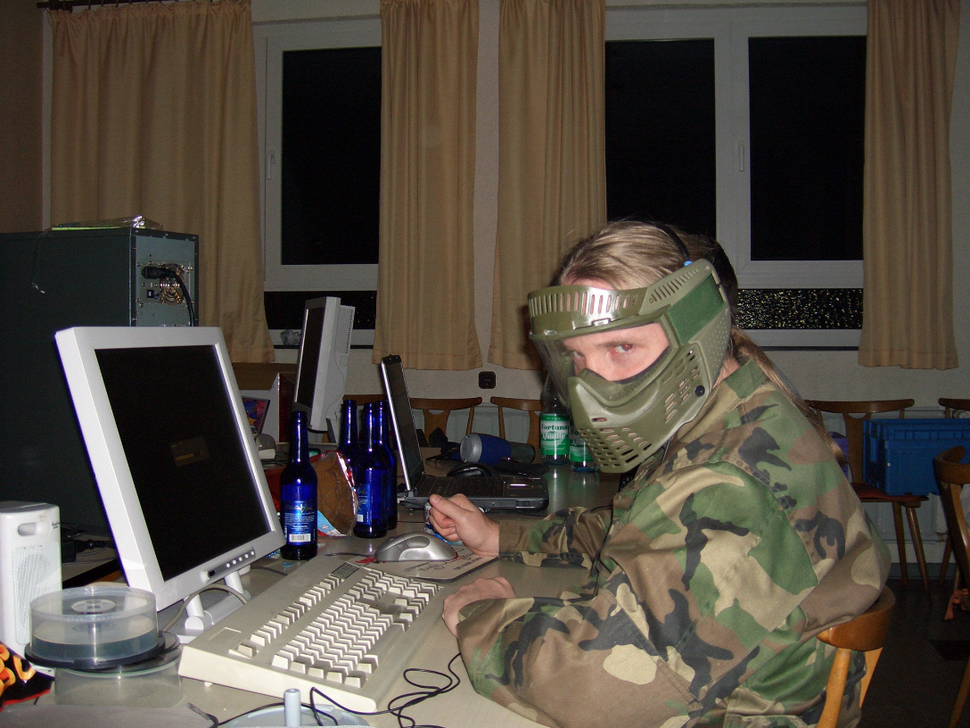 a dude in a camo jacket and green mask in front of an old-school computer monitor