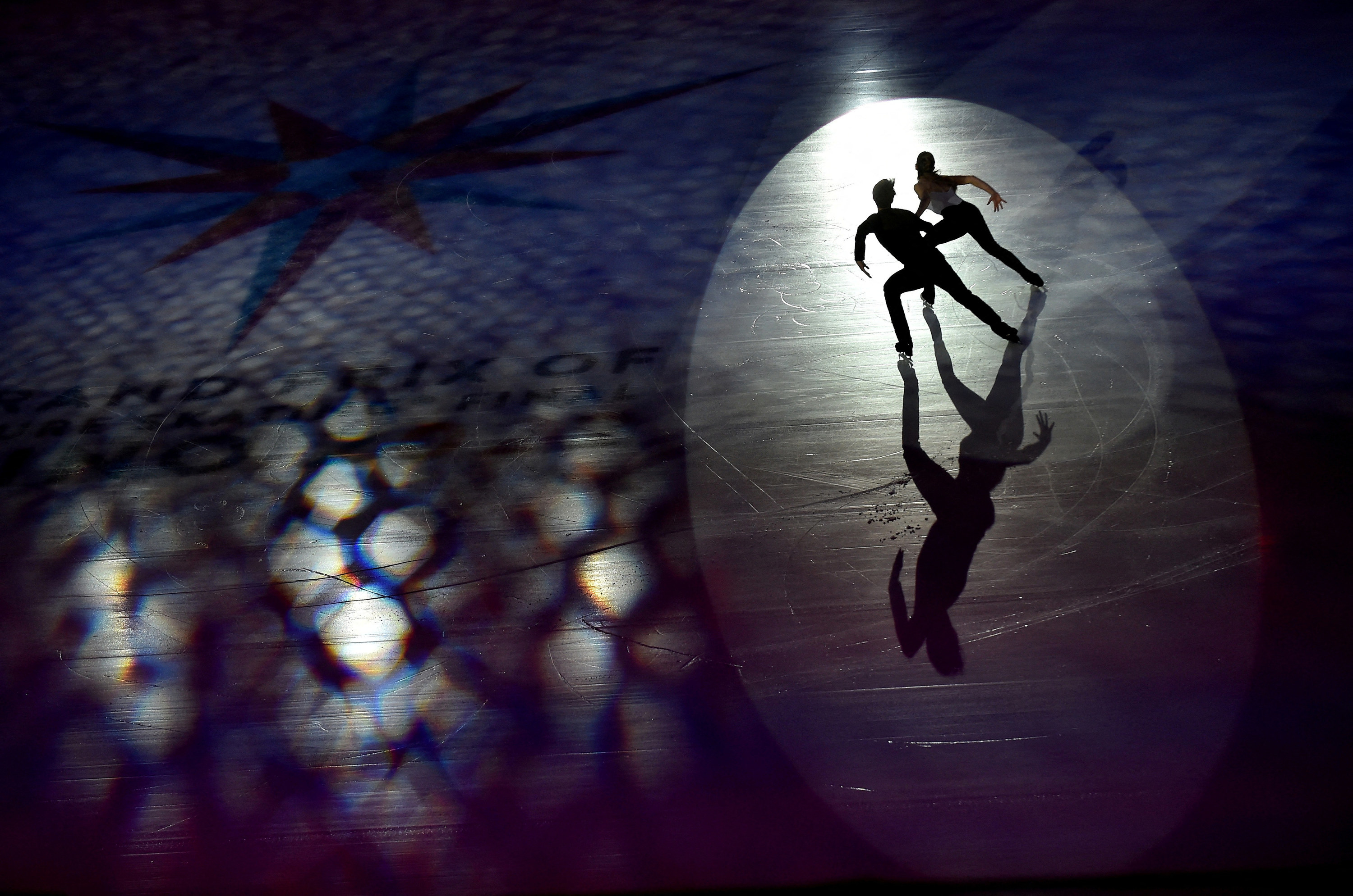 On a darkened ice rink stage, two figure skaters dance side by side