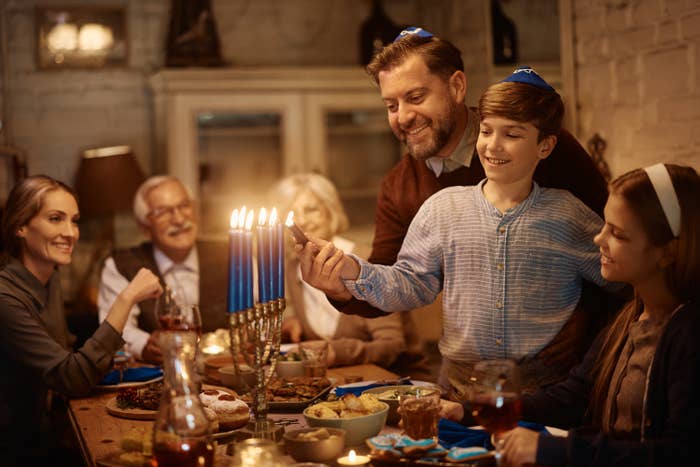 Happy Jewish boy and his father lighting candles in menorah during family dinner at dining table on Hanukkah