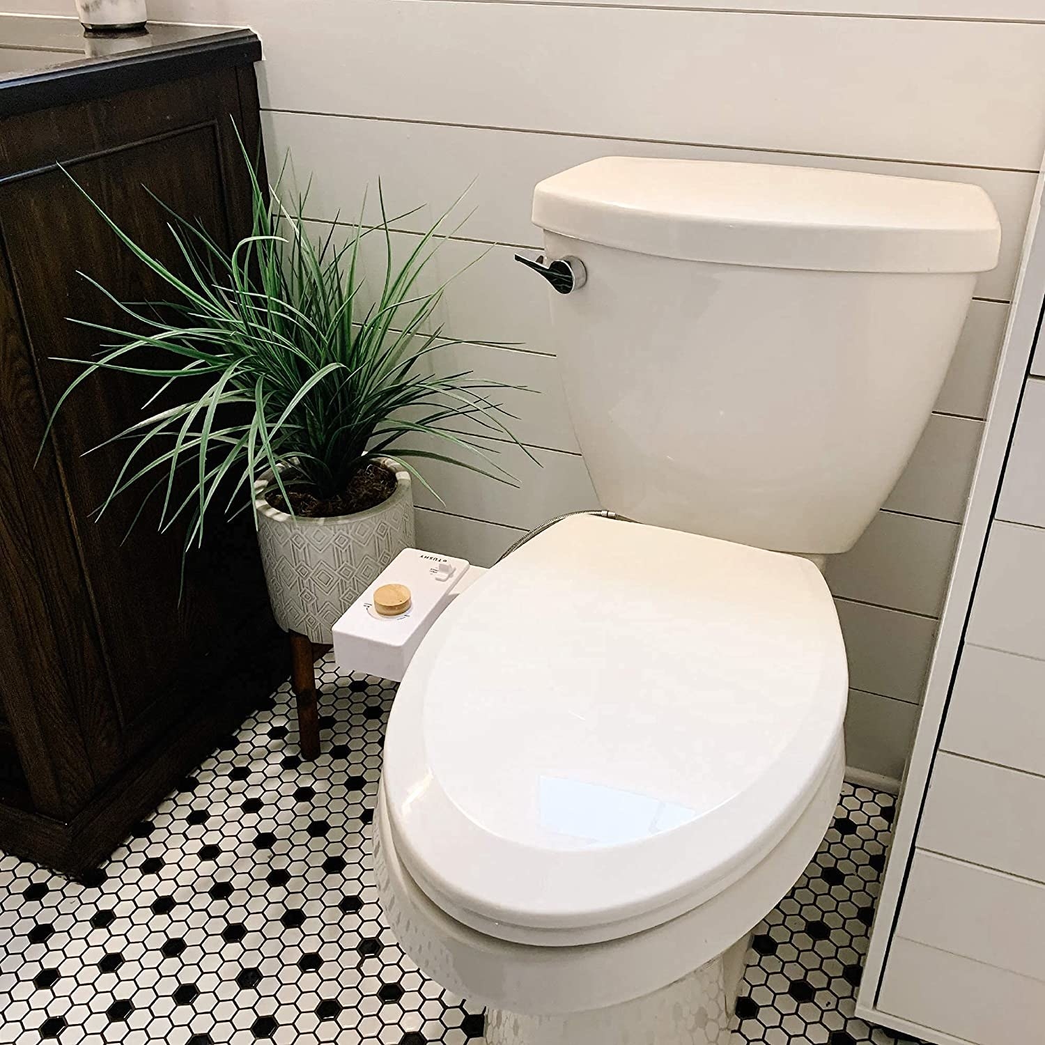 The attachment on a toilet in a modern bathroom with hexagonal tiles and a plant