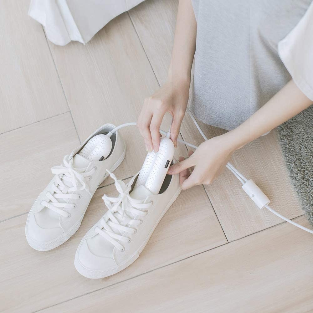 a person inserting two oval-shaped vented shoe dryers into a pair of sneakers
