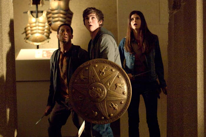 three teens holding weapons and shields looking up