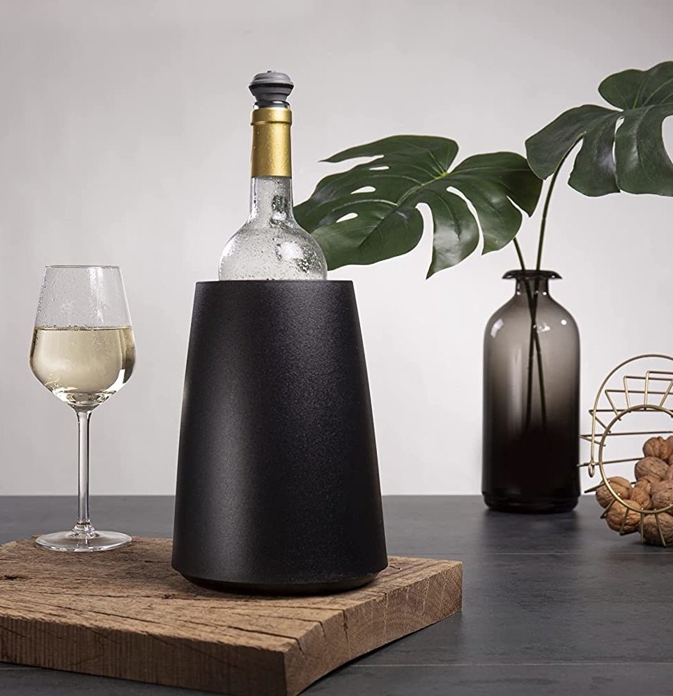 a tabletop wine chiller next to a wine glass and a leafy arrangement
