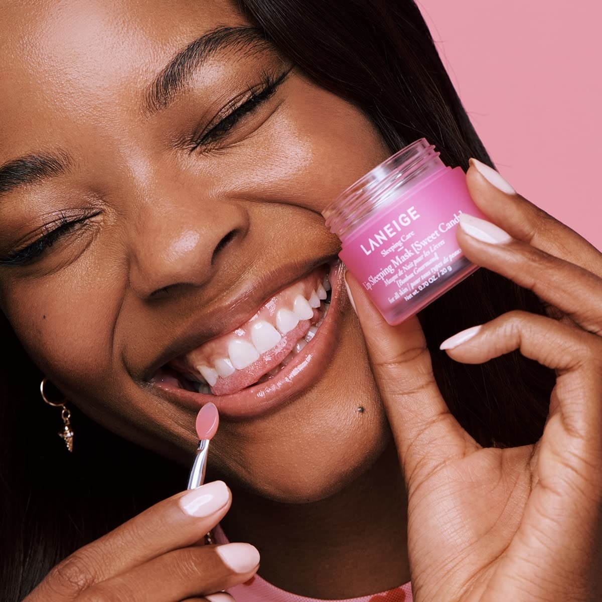 model holding the jar of product and smiling applying the lip mask to their lips with an applicator