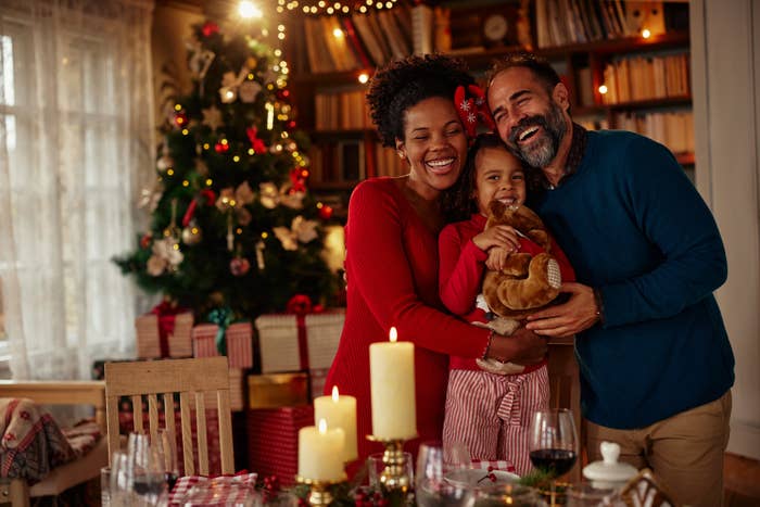 Mixed race parents and daughter standing around dining table, hugging, smiling and enjoying holiday together