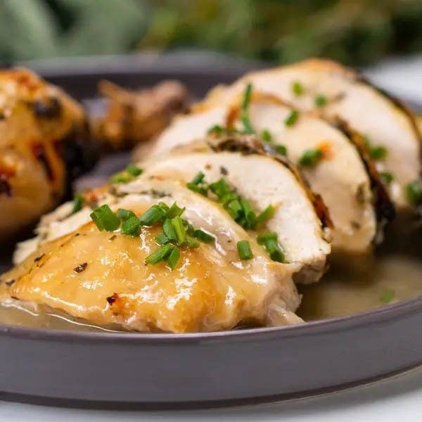 Close-up of sliced roasted chicken breast garnished with chopped herbs on a plate