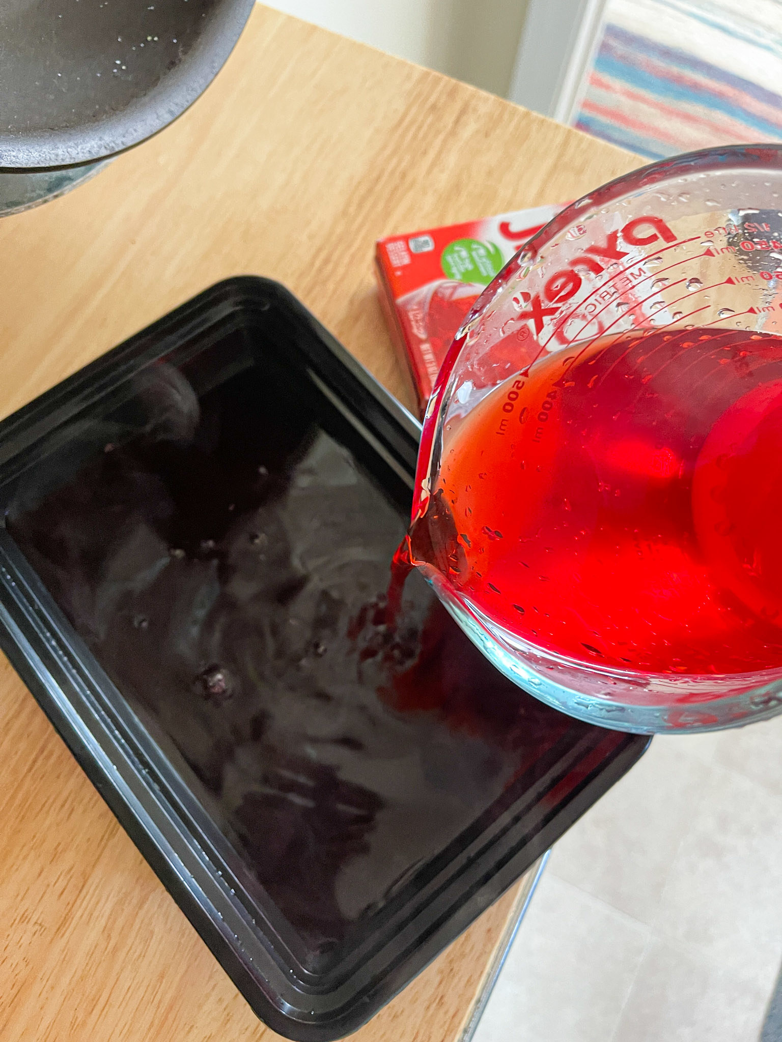 pouring strawberry jello mix into black tupperware