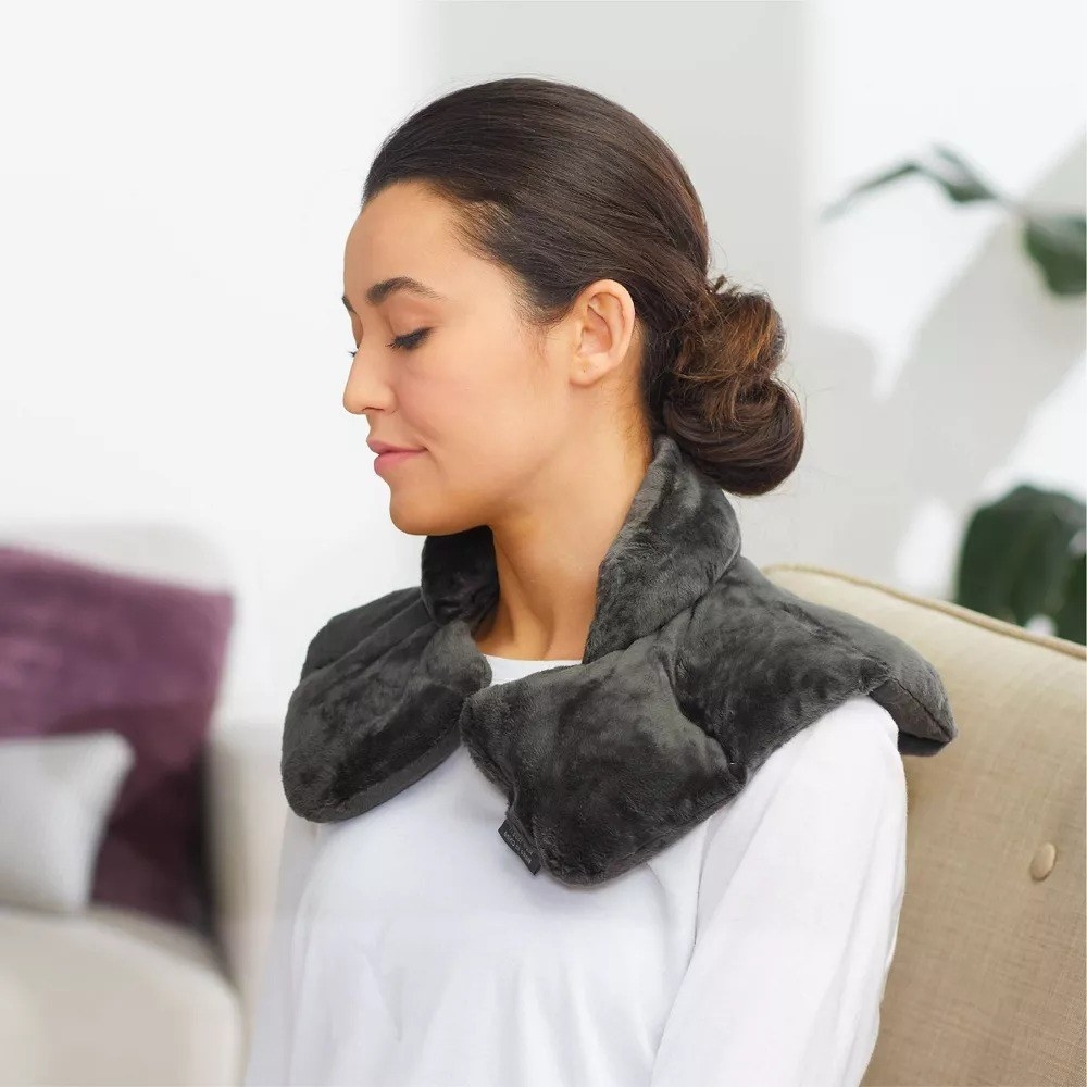 A woman relaxing on a couch with the fleece neck wrap around her shoulders