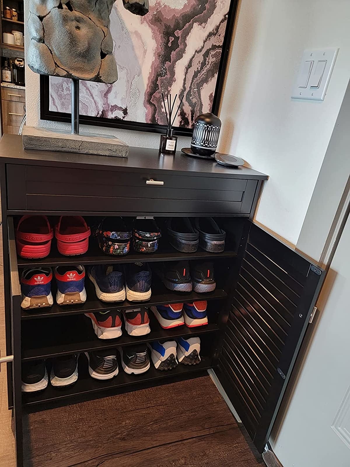 the furniture  open, revealing 4  shelves with 3  pairs of big  shoes each