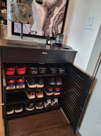 the furniture open, revealing 4 shelves with 3 pairs of big shoes each