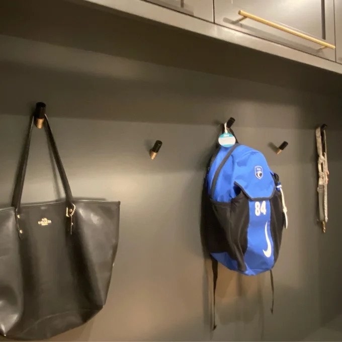 Black hooks on wall with black purse and blue backpack hanging on them
