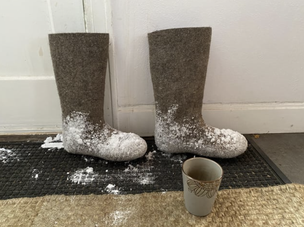Calf-high boots with snow on them on a mat