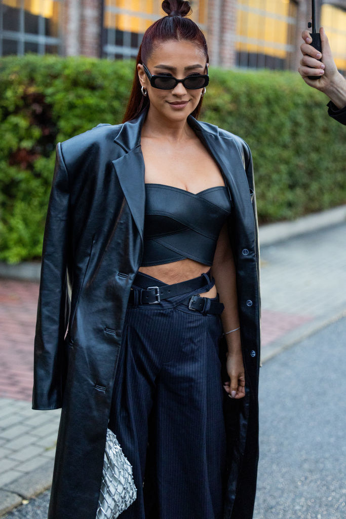 Shay Mitchell in trousers and a leather crop top and long jacket