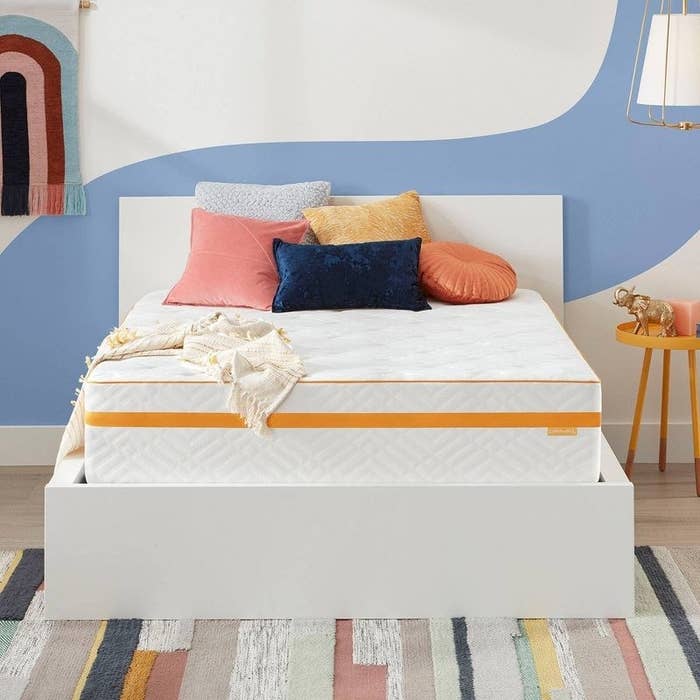 A white mattress on a white bed with yellow stripe and colorful pillows