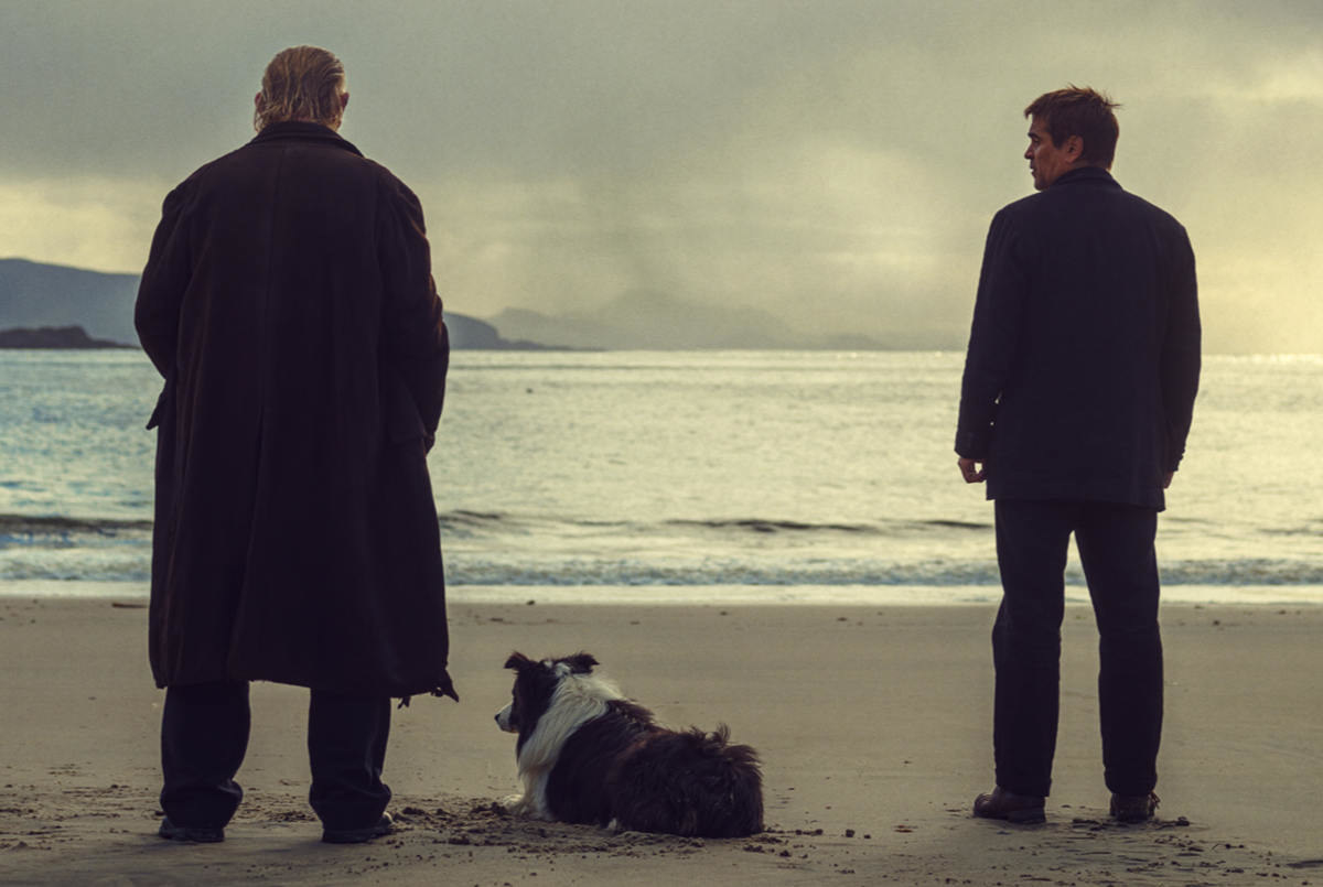 A still from the movie &quot;The Banshees of Inisherin.&quot; Two men stand on a beach looking out into the water. A dog lays next to the older man.