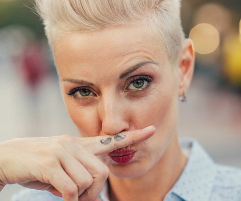 a woman holding up a mustache finger tattoo to her face
