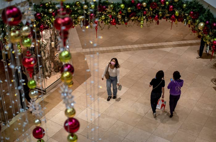 A woman wearing a mask looks up at festive christmas decorations at an area mall
