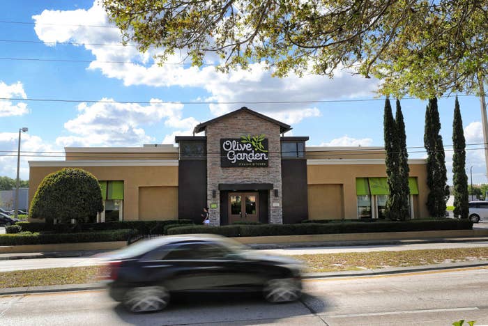 A blurry car drives by an Olive Garden restaurant