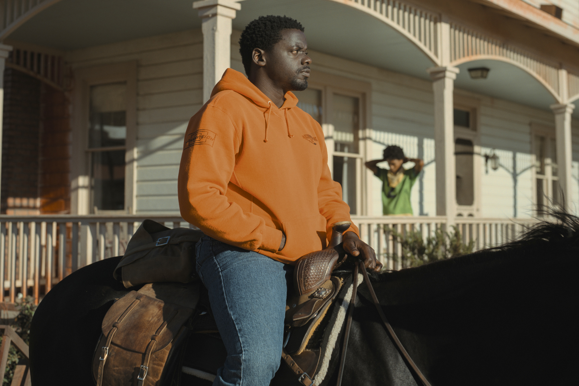 Daniel Kaluuya as OJ Haywood rides on the back of a horse while Keke Palmer as Em Haywood stands behind on the porch of a house.
