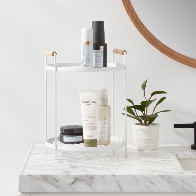 The white two tiered organizer is holding some beauty products
