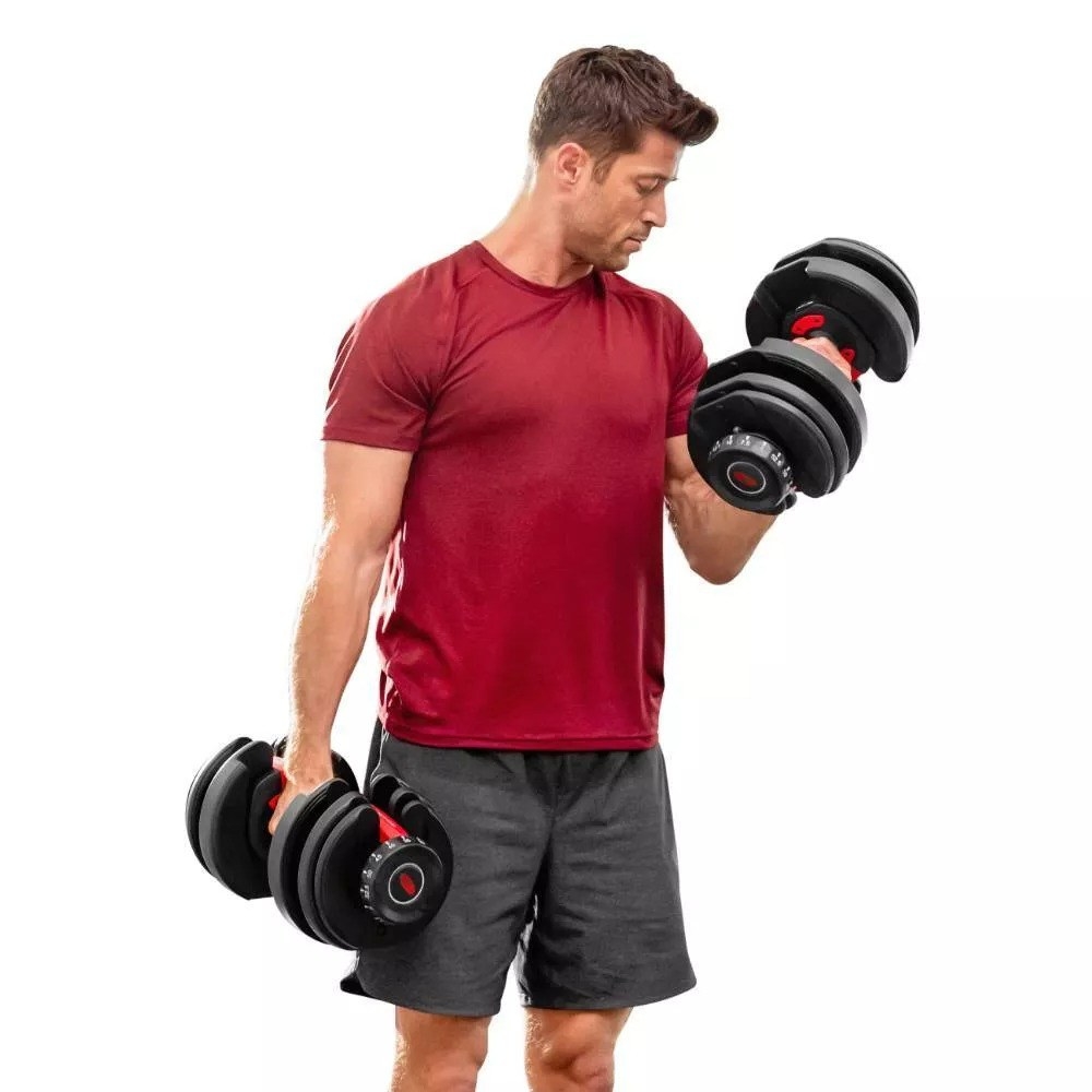 A man in a red shirt and black shorts exercising with two of the dumbbells
