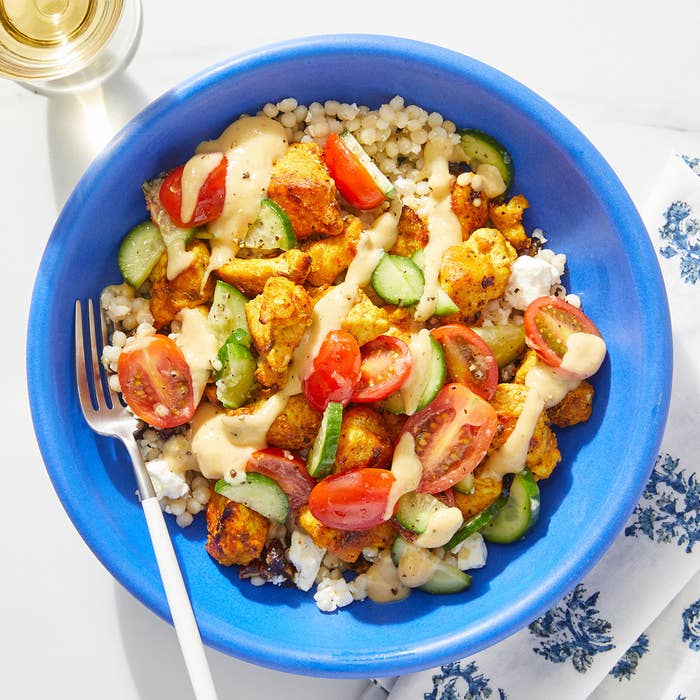shawarma chicken and couscous in a bowl with vegetables and tahini sauce drizzled on top