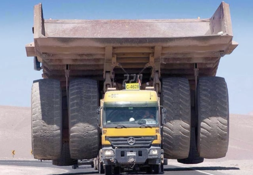 truck towing a very large truck with two large tires sandwiching the truck in the front