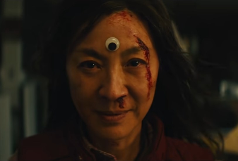 Michelle Yeoh as Evelyn Wang with a bloodied face smirking as a plastic arts and crafts eye is one her forehead